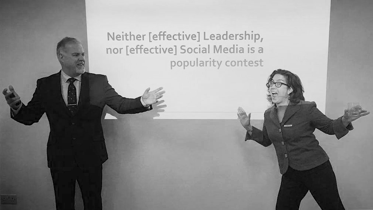 Lawrie Phipps and Donna Lanclose standing in front of a screen. The Screens reads: "Niether (effective) leadership; nor (effective) social media is a popularity contest"
