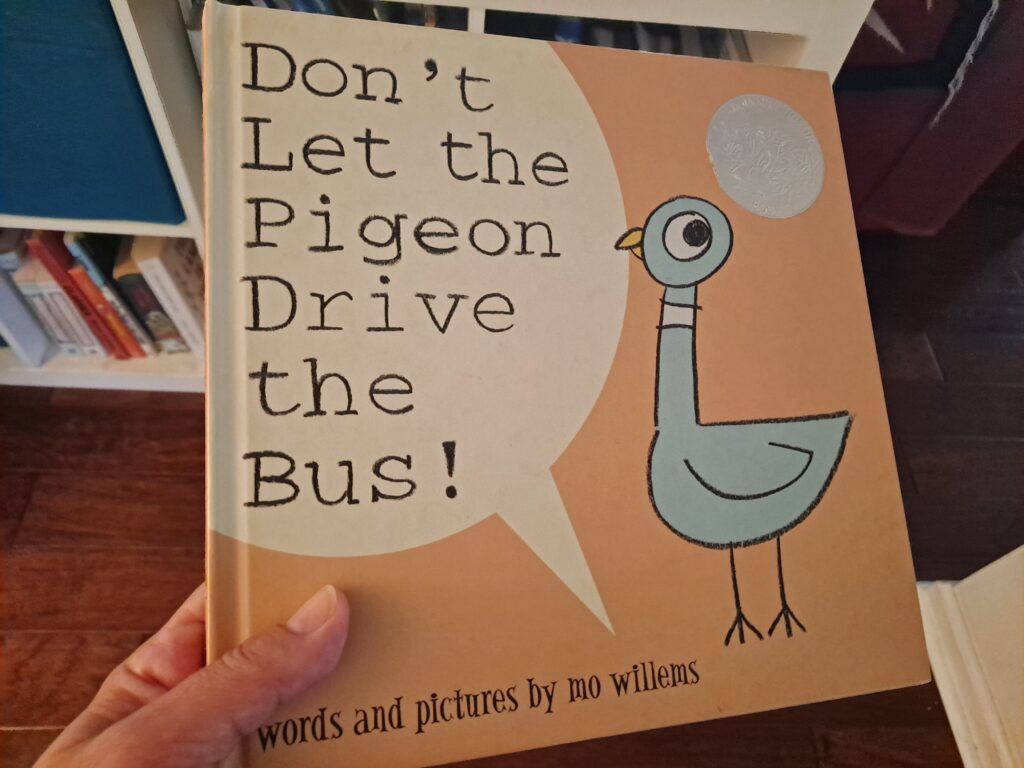 a hand holding a hardback copy of the book Don't Let the Pigeon Drive the Bus, by Mo Willems